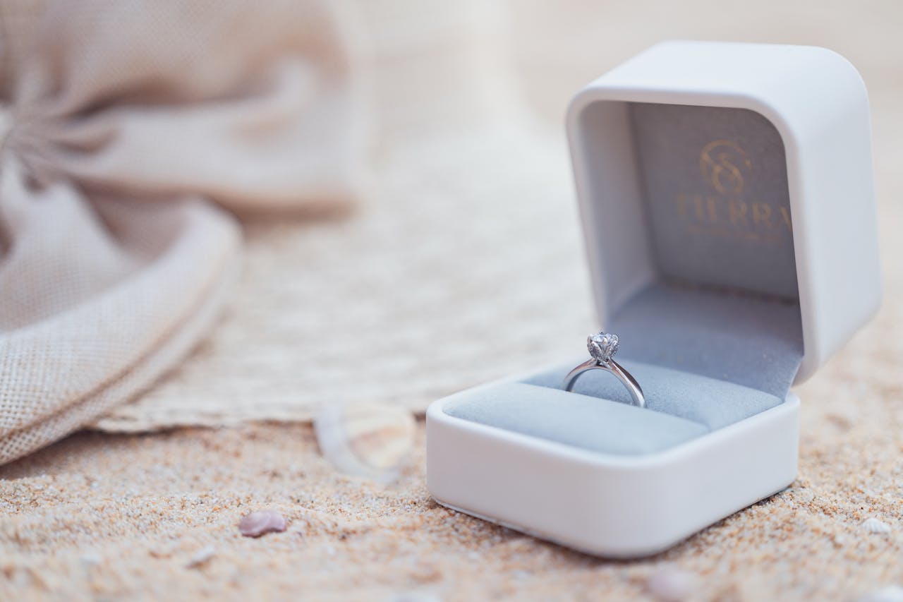 A stunning silver engagement ring elegantly displayed in a box on a sandy beach.