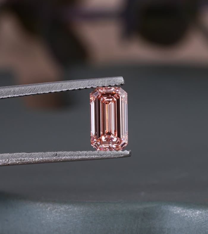 Close-up of a pink emerald cut diamond held in tweezers, showcasing its brilliance and cut.